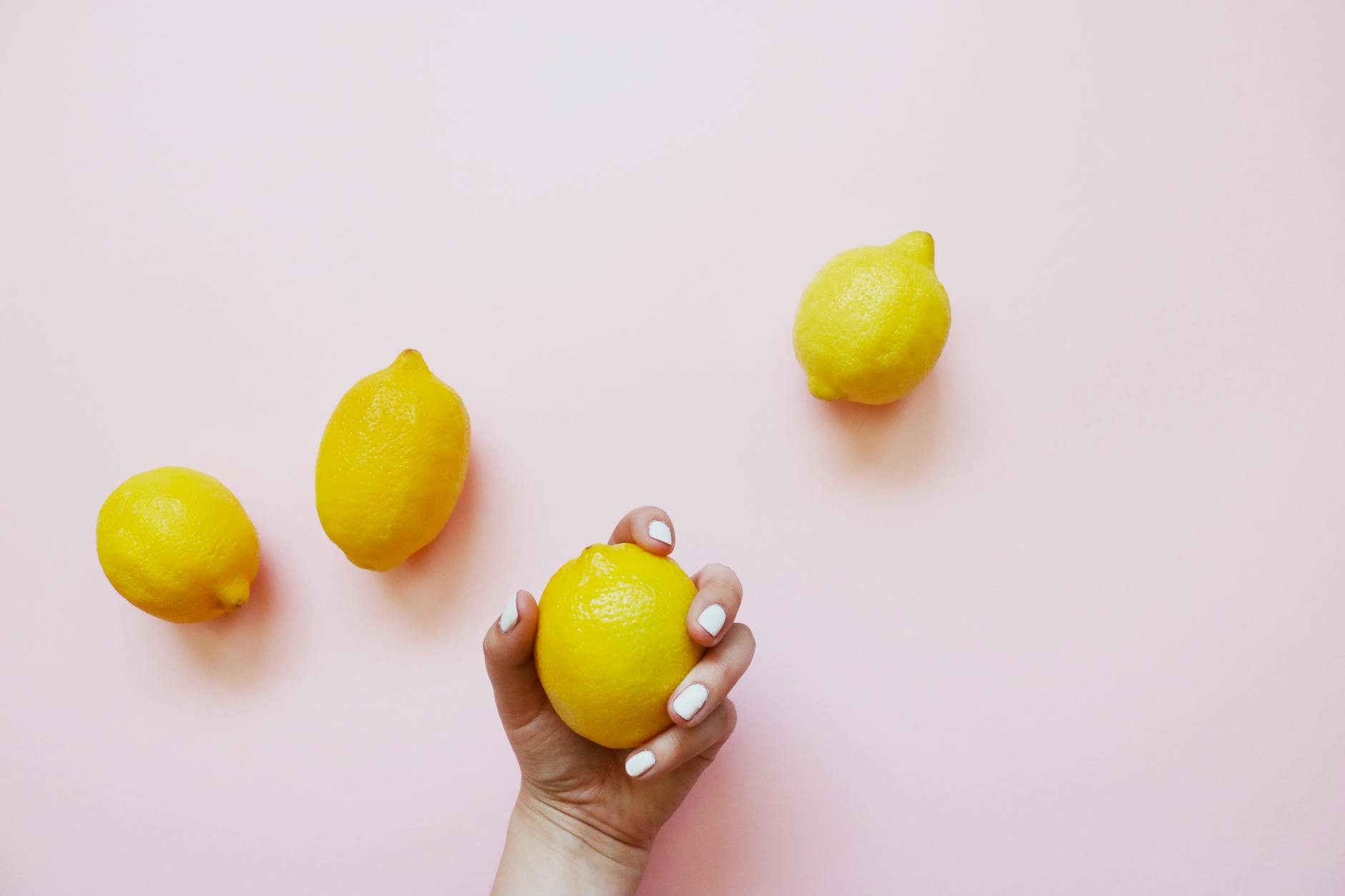 A hand holding a fresh lemon on a soft pink background, symbolizing sensitivity and natural rhythm