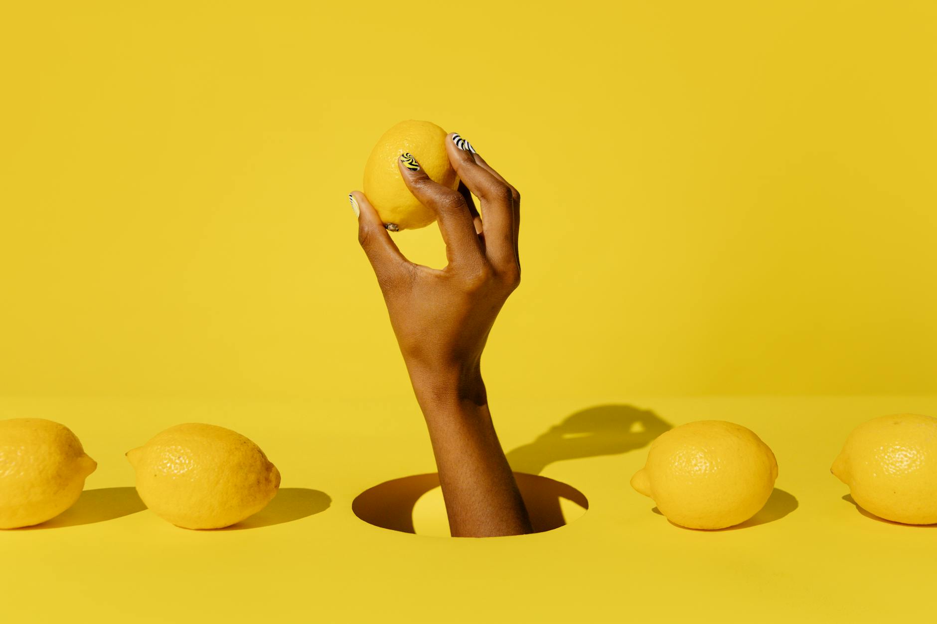 A hand holding a fresh lemon against a vibrant yellow background, symbolizing reconnection and citrus-bright sensation.