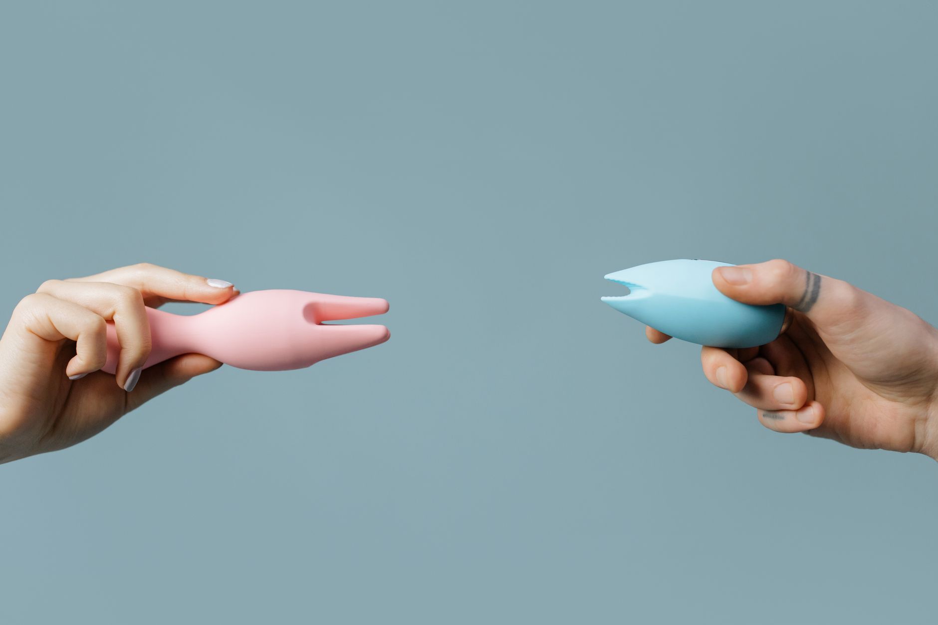 Two hands holding colorful vibrators against a pastel background, representing fresh starts and sexual confidence.