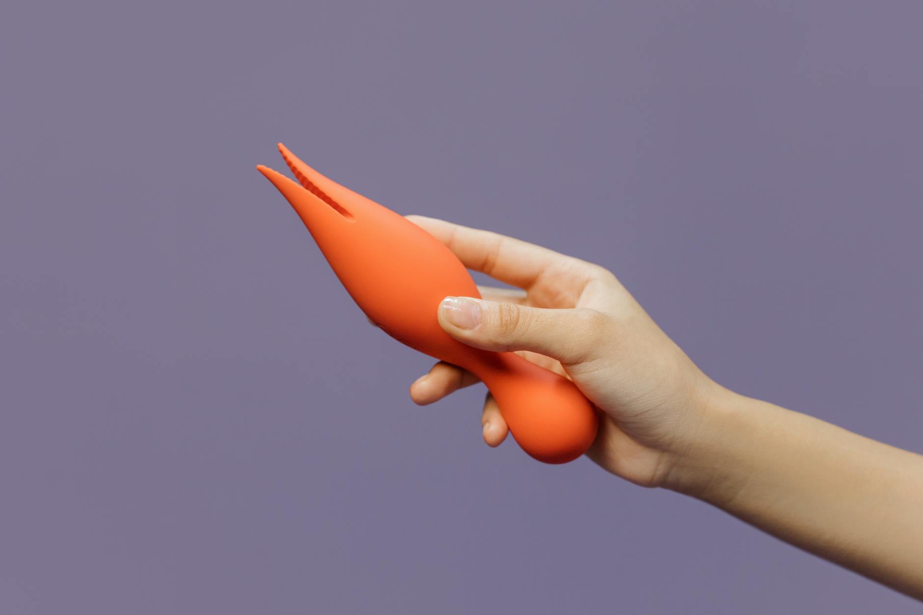 Close-up of a hand holding an orange vibrator against a minimalistic backdrop, symbolizing sensual touch and pleasure recovery