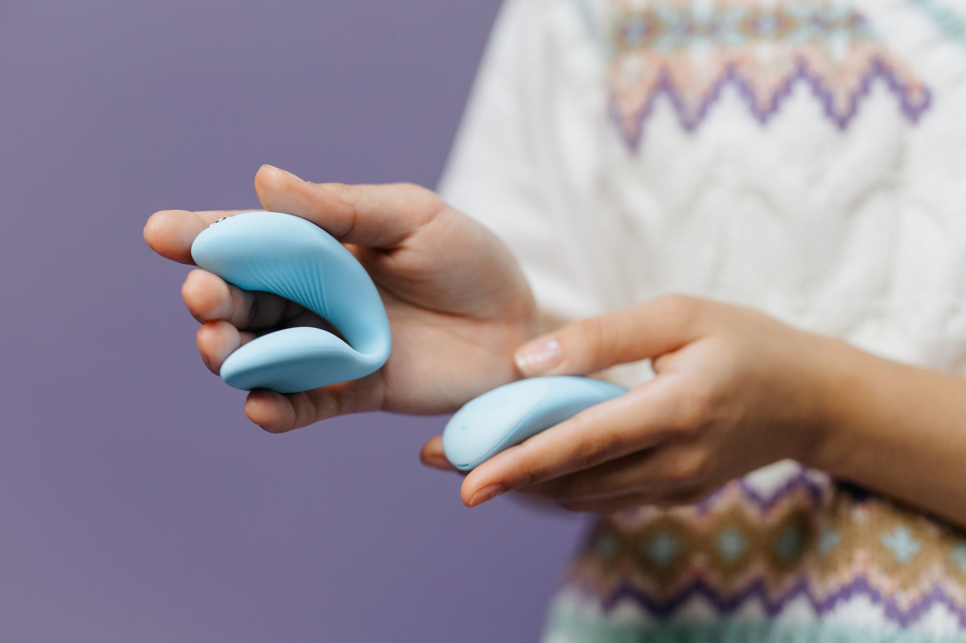 Mano sosteniendo un vibrador azul elegante contra un fondo púrpura, simbolizando placer y bienestar