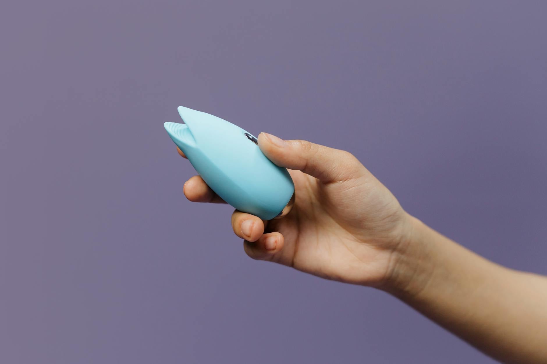 A silicone vibrator held gently in hand against a purple background, symbolizing self-care and reconnection with pleasure