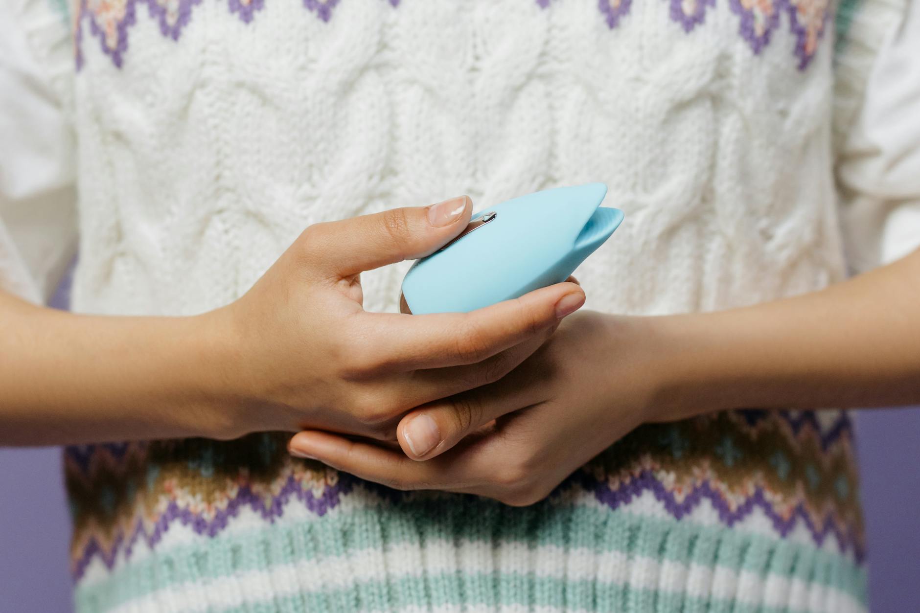 Hands holding a lemon vibrator against a knitted sweater in soft lighting