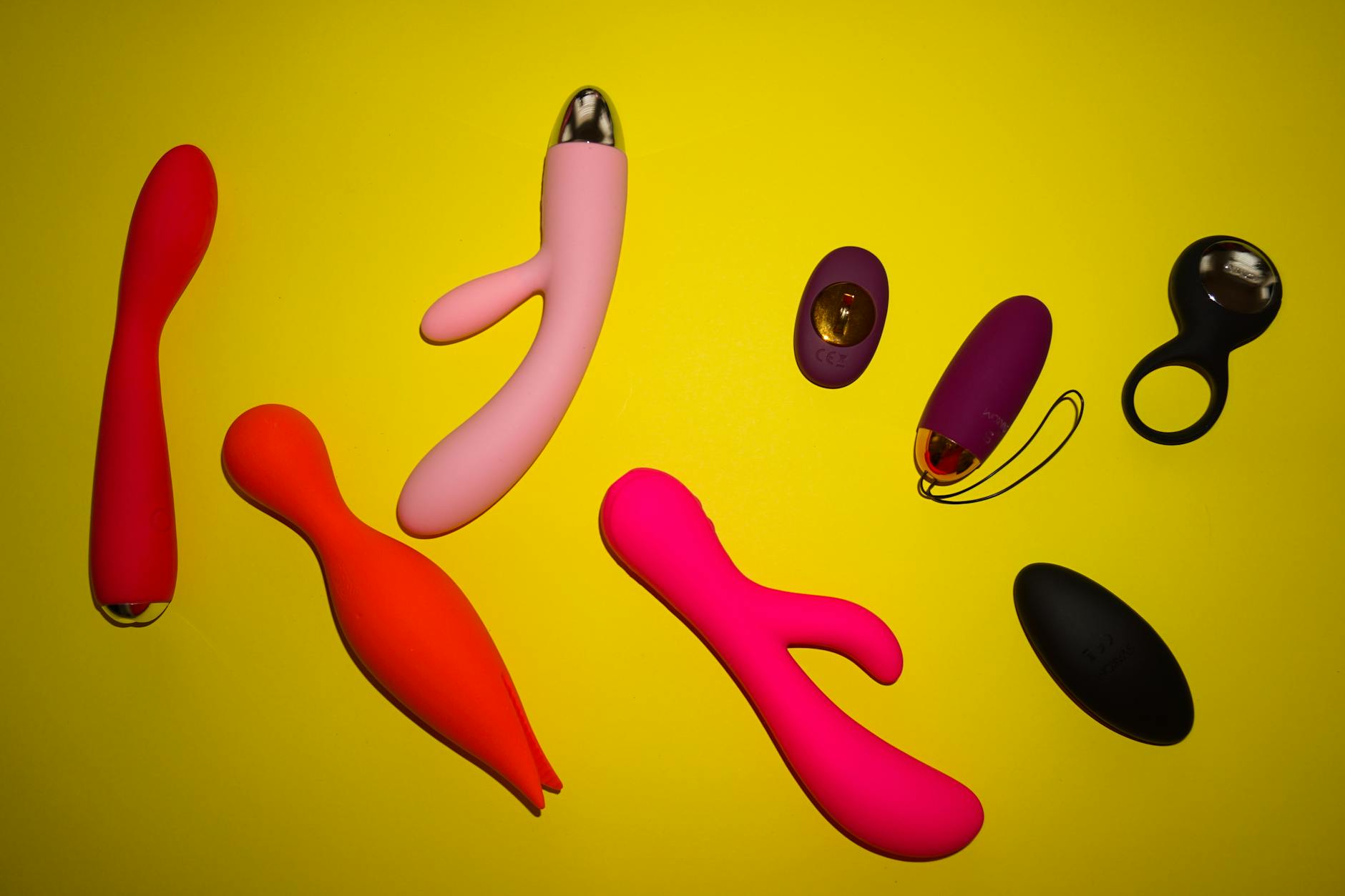 Various colorful vibrators arranged on a bright yellow background, showcasing different design options
