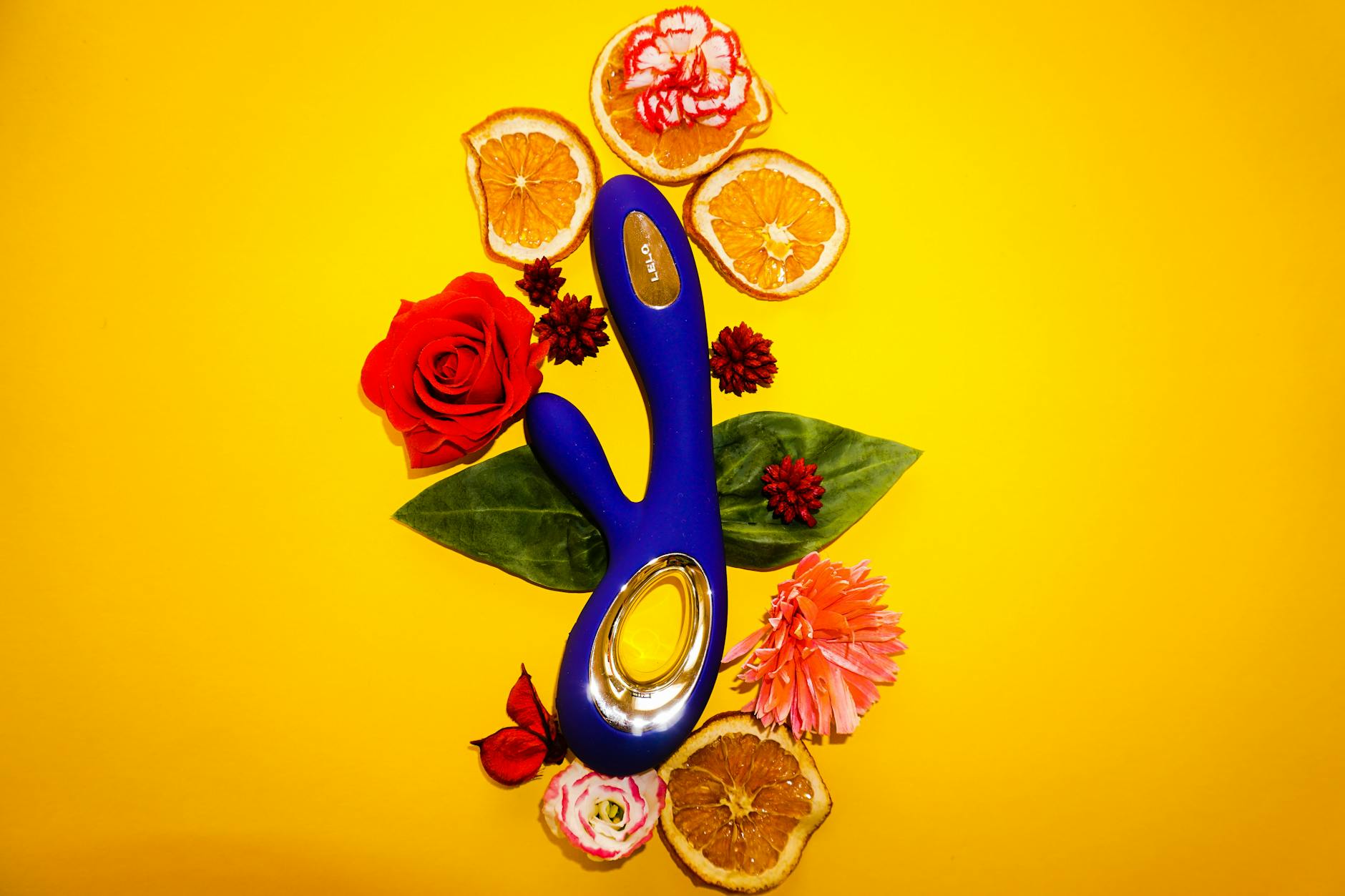 A blue clitoral vibrator surrounded by citrus and flowers on a bright background