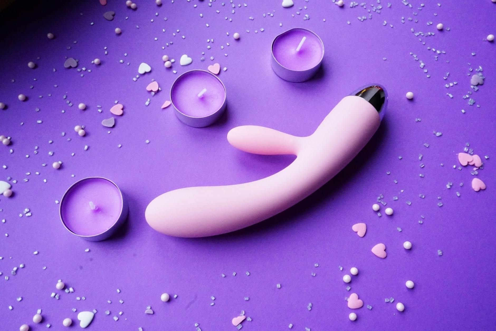 Pink lemon clitoral vibrator on purple background with romantic candles and heart confetti